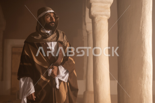 رجل كبير السن عربي سعودي خليجي يرتدي البشت وعقال يوم التأسيس يقف  داخل مبنى طيني تفاصيل العمارة القديمة, ذكرى تأسيس الدوله السعوديه الاولى على يد الامام محمد بن سعود, يوم بدينا 22 فبراير 1727م, العمق التاريخي والحضاري للمملكة، ارتداء الأزياء التقليدية تعكس التراث