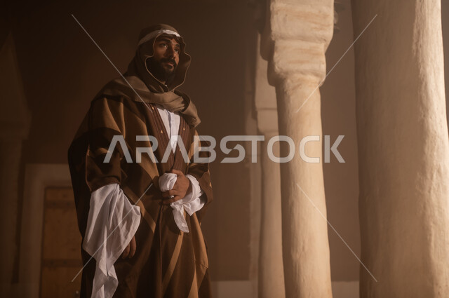 صورة من الخلف لرجل كبير السن عربي سعودي خليجي يرتدي البشت وعقال يوم التأسيس يقف  داخل مبنى طيني تفاصيل العمارة القديمة, ذكرى تأسيس الدوله السعوديه الاولى على يد الامام محمد بن سعود, يوم بدينا 22 فبراير 1727م, العمق التاريخي والحضاري للمملكة، ارتداء الأزياء التقليدية تعكس التراث
