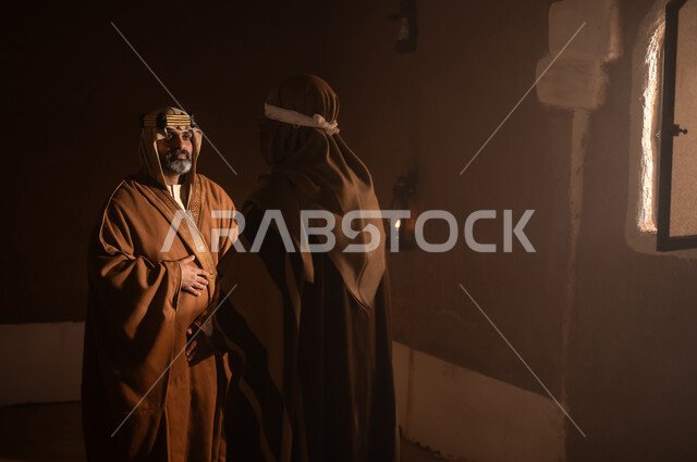 رجل كبير السن عربي سعودي خليجي يرتدي البشت وعقال يوم التأسيس يتحدث داخل مبنى طيني مع رجل, ذكرى تأسيس الدوله السعوديه الاولى على يد الامام محمد بن سعود, يوم بدينا 22 فبراير 1727م, العمق التاريخي والحضاري للمملكة، ارتداء الأزياء التقليدية تعكس التراث