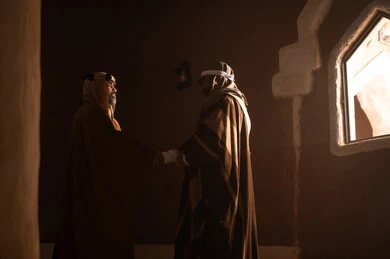 رجل كبير السن عربي سعودي خليجي يرتدي البشت وعقال يوم التأسيس يتحدث داخل مبنى طيني مع رجل, ذكرى تأسيس الدوله السعوديه الاولى على يد الامام محمد بن سعود, يوم بدينا 22 فبراير 1727م, العمق التاريخي والحضاري للمملكة، ارتداء الأزياء التقليدية تعكس التراث