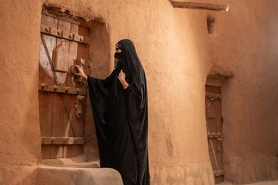 ارتداء الزي الشعبي في ذكرى تأسيس الدولة السعودية الاولى 22 فبراير، الفخر والاعتزاز بالهوية الوطنية، نمط حياة البدو الشعبية في البيوت الطينية التراثية، يوم بدينا 1727 م، امرأة عربية خليجية سعودية ترتدي العباءة السوداء والبرقع في منزل قديم