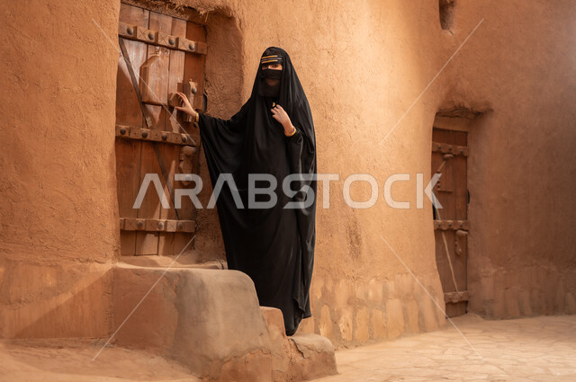 ارتداء الزي الشعبي في ذكرى تأسيس الدولة السعودية الاولى 22 فبراير، الفخر والاعتزاز بالهوية الوطنية، نمط حياة البدو الشعبية في البيوت الطينية التراثية، يوم بدينا 1727 م، امرأة عربية خليجية سعودية ترتدي العباءة السوداء والبرقع في منزل قديم