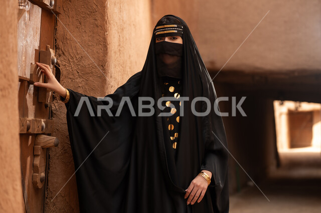 ارتداء الزي الشعبي في ذكرى تأسيس الدولة السعودية الاولى 22 فبراير، الفخر والاعتزاز بالهوية الوطنية، نمط حياة البدو الشعبية في البيوت الطينية التراثية، يوم بدينا 1727 م، امرأة عربية خليجية سعودية ترتدي العباءة السوداء والبرقع في منزل قديم