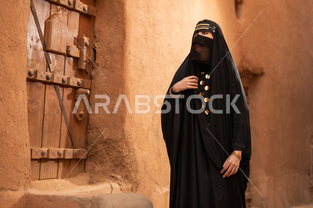 ارتداء الزي الشعبي في ذكرى تأسيس الدولة السعودية الاولى 22 فبراير، الفخر والاعتزاز بالهوية الوطنية، نمط حياة البدو الشعبية في البيوت الطينية التراثية، يوم بدينا 1727 م، امرأة عربية خليجية سعودية ترتدي العباءة السوداء والبرقع في منزل قديم