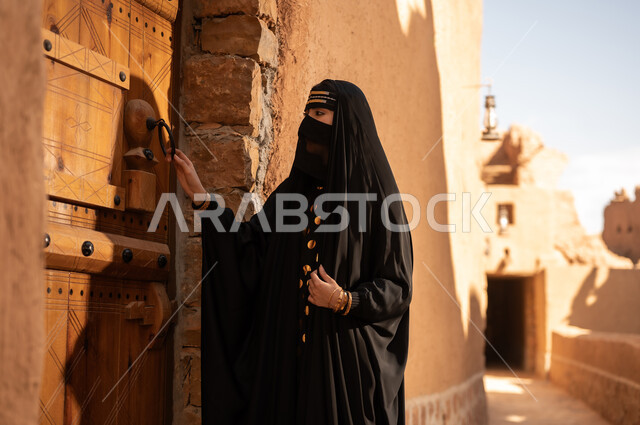 الفخر والاعتزاز بالهوية الوطنية، نمط حياة البدو الشعبية في البيوت الطينية التراثية، يوم بدينا 1727 م، ارتداء الزي الشعبي في ذكرى تأسيس الدولة السعودية الاولى 22 فبراير، امرأة عربية خليجية سعودية ترتدي العباءة السوداء والبرقع في منزل قديم