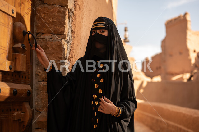 ارتداء الزي الشعبي في ذكرى تأسيس الدولة السعودية الاولى 22 فبراير، الفخر والاعتزاز بالهوية الوطنية، نمط حياة البدو الشعبية في البيوت الطينية التراثية، يوم بدينا 1727 م، امرأة عربية خليجية سعودية ترتدي العباءة السوداء والبرقع في منزل قديم