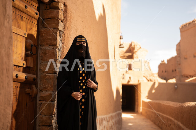 الفخر والاعتزاز بالهوية الوطنية، نمط حياة البدو الشعبية في البيوت الطينية التراثية، يوم بدينا 1727 م، ارتداء الزي الشعبي في ذكرى تأسيس الدولة السعودية الاولى 22 فبراير، امرأة عربية خليجية سعودية ترتدي العباءة السوداء والبرقع في منزل قديم