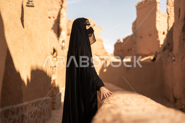 ارتداء الزي الشعبي في ذكرى تأسيس الدولة السعودية الاولى 22 فبراير، الفخر والاعتزاز بالهوية الوطنية، نمط حياة البدو الشعبية في البيوت الطينية التراثية، يوم بدينا 1727 م، امرأة عربية خليجية سعودية ترتدي العباءة السوداء والبرقع في منزل قديم