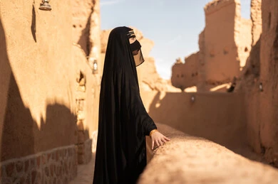 ارتداء الزي الشعبي في ذكرى تأسيس الدولة السعودية الاولى 22 فبراير، الفخر والاعتزاز بالهوية الوطنية، نمط حياة البدو الشعبية في البيوت الطينية التراثية، يوم بدينا 1727 م، امرأة عربية خليجية سعودية ترتدي العباءة السوداء والبرقع في منزل قديم