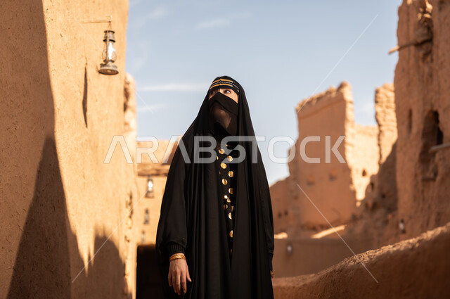 الفخر والاعتزاز بالهوية الوطنية، نمط حياة البدو الشعبية في البيوت الطينية التراثية، يوم بدينا 1727 م، ارتداء الزي الشعبي في ذكرى تأسيس الدولة السعودية الاولى 22 فبراير، امرأة عربية خليجية سعودية ترتدي العباءة السوداء والبرقع في منزل قديم