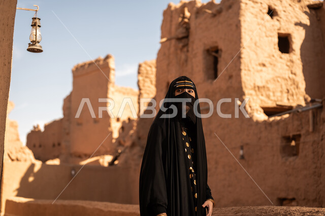 ارتداء الزي الشعبي في ذكرى تأسيس الدولة السعودية الاولى 22 فبراير، الفخر والاعتزاز بالهوية الوطنية، نمط حياة البدو الشعبية في البيوت الطينية التراثية، يوم بدينا 1727 م، امرأة عربية خليجية سعودية ترتدي العباءة السوداء والبرقع في منزل قديم