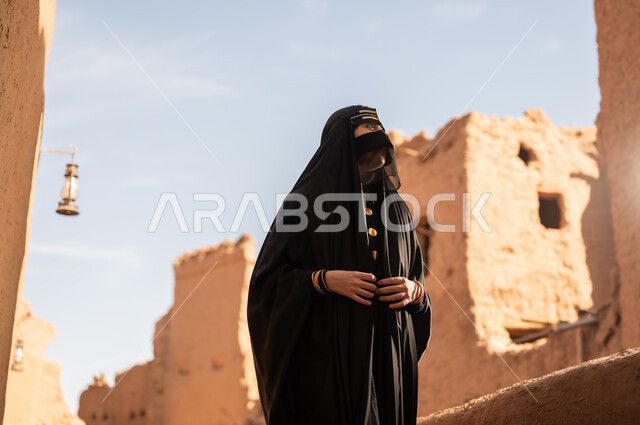 الفخر والاعتزاز بالهوية الوطنية، نمط حياة البدو الشعبية في البيوت الطينية التراثية، يوم بدينا 1727 م، ارتداء الزي الشعبي في ذكرى تأسيس الدولة السعودية الاولى 22 فبراير، امرأة عربية خليجية سعودية ترتدي العباءة السوداء والبرقع في منزل قديم