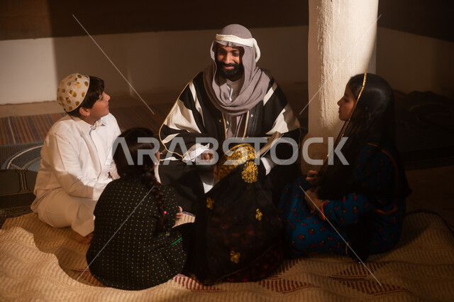 A story for the children, sitting in one of the traditional mud houses, on the day we began in 1727 AD, the love among family members, the anniversary of the founding of the first Saudi state on February 22, an Arab Gulf Saudi man sitting with his children wearing traditional costumes during national holidays.