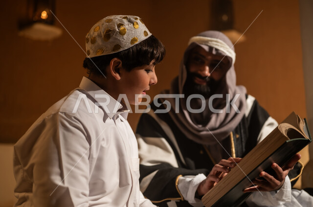 Sitting in one of the traditional mud houses, on the day we began in 1727 AD, telling a story to the children, the love among family members, the anniversary of the founding of the first Saudi state on February 22, an Arab Gulf Saudi man sitting with his son, both wearing traditional attire during national holidays.