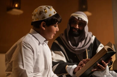 Sitting in one of the traditional mud houses, on the day we began in 1727 AD, telling a story to the children, the love among family members, the anniversary of the founding of the first Saudi state on February 22, an Arab Gulf Saudi man sitting with his son, both wearing traditional attire during national holidays.