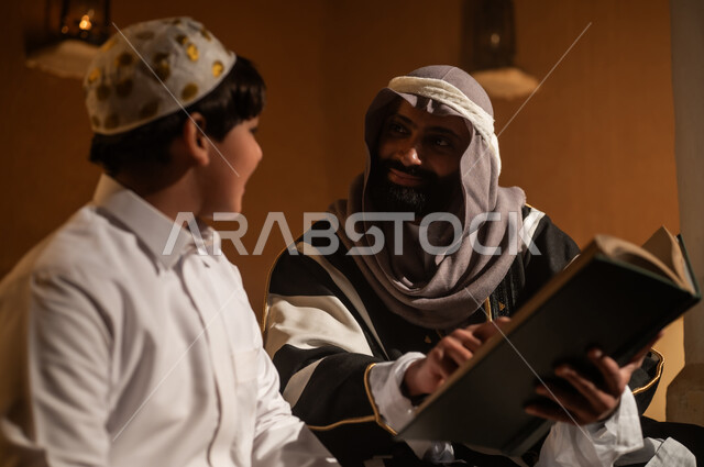 الجلوس في احدى البيوت التراثية الطينية ،يوم بدينا 1727 م ، رواية قصة للابناء، المحبة بين افراد الأسرة ،ذكرى تأسيس الدولة السعودية الأولى 22 فبراير ، رجل عربي خليجي سعودي يجلس مع ابنه يرتديان الأزياء الشعبية في الأعياد الوطنية