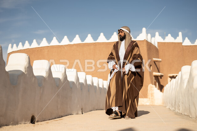 رجل عربي خليجي سعودي يرتدي زي تراثي سعودي للمناسبات الوطنية، يوم التأسيس السعودي، تأسيس المملكة 1727م ، أزياء شعبية سعودية، تصميم معماري عربي قديم، بيوت طينية تراثية قديمة ، يوم بدينا ٢٢فبراير