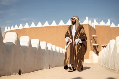 رجل عربي خليجي سعودي يرتدي زي تراثي سعودي للمناسبات الوطنية، يوم التأسيس السعودي، تأسيس المملكة 1727م ، أزياء شعبية سعودية، تصميم معماري عربي قديم، بيوت طينية تراثية قديمة ، يوم بدينا ٢٢فبراير