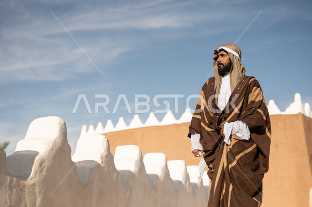 رجل عربي خليجي سعودي يرتدي زي تراثي سعودي للمناسبات الوطنية، يوم التأسيس السعودي، تأسيس المملكة 1727م ، أزياء شعبية سعودية، تصميم معماري عربي قديم، بيوت طينية تراثية قديمة ، يوم بدينا ٢٢فبراير