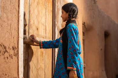 A Gulf Arab Saudi girl wearing traditional attire is opening an old wooden door, commemorating the founding of the first Saudi state by Imam Muhammad bin Saud, on the day we began, February 22, 1727. The historical and cultural depth of the Kingdom, wearing traditional costumes reflects the heritage.