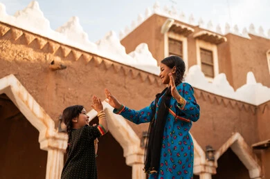 A Saudi Arabian Gulf girl wearing traditional attire plays with her sister in an old mud neighborhood, commemorating the founding of the first Saudi state by Imam Muhammad bin Saud, on the day we began, February 22, 1727. The historical and cultural depth of the Kingdom, wearing traditional costumes reflects the heritage.
