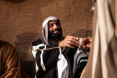 The hospitality and generosity of the Bedouins, the day we began in 1727 AD, a popular neighborhood with traditional mud houses, the anniversary of the establishment of the first Saudi state on February 22, expressing love and loyalty to the state and the homeland, an Arab Gulf Saudi man wearing traditional folk attire serving Arabic coffee, pride and honor in national identity.