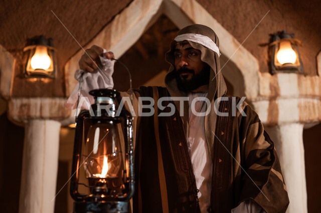 عيد ومناسبة وطنية، ذكرى تأسيس الدولة السعودية الاولى 22 فبراير, إظهار الحب والولاء للدولة والوطن, رجل عربي خليجي سعودي يرتدي زي شعبي تراثي يحمل بيده فانوس مضيء، فخر واعتزاز بالهوية الوطنية, يوم بدينا 1727 م, حي شعبي وبيوت طينية تراثية