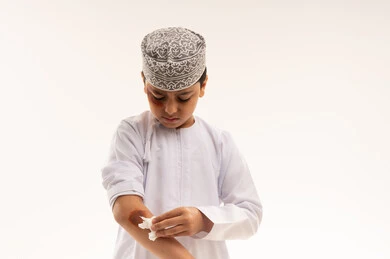 طفل عماني ينظف إصابة في ذراعه بخلفية بيضاء