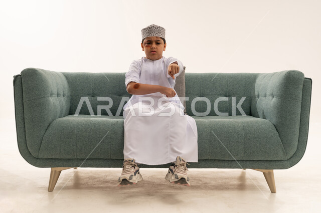 Omani Boy in Traditional Dress Pointing on Green Sofa