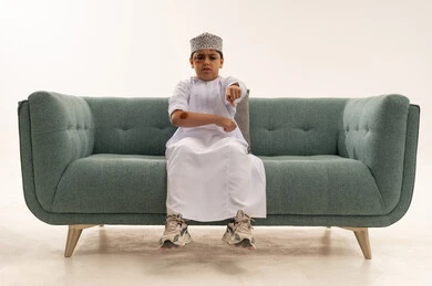 Omani Boy in Traditional Dress Pointing on Green Sofa