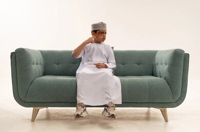 طفل عماني بالدشداشة التقليدية على أريكة حديثة