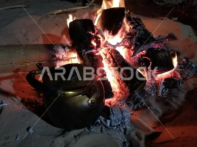 صورة لإبريق الشاي على النار ، حرق خشب الشجر ، رحلات برية ، أجواء شتوية ، رحلة برية في صحراء المملكة العربية السعودية ، جلسة بر عربية شعبية مع شعلة الحطب في صحراء السعودية ، براد شاي على الحطب