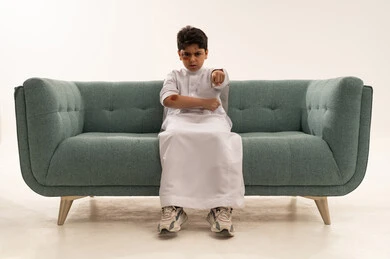 طفل سعودي بالثوب الأبيض يشير بغضب على أريكة