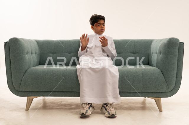 طفل سعودي بالثوب الأبيض على أريكة خضراء