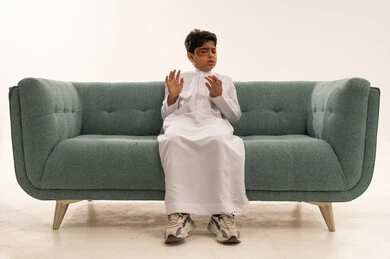 طفل سعودي بالثوب الأبيض على أريكة خضراء