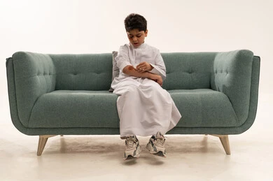 Saudi Boy in Thobe Cleaning Arm Wound on Sofa
