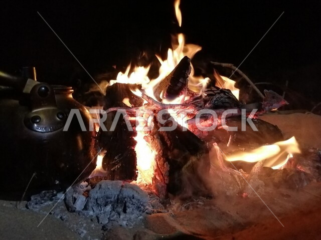 صورة لإبريق الشاي على النار ، حرق خشب الشجر ، رحلات برية ، أجواء شتوية ، رحلة برية في صحراء المملكة العربية السعودية ، جلسة بر عربية شعبية مع شعلة الحطب في صحراء السعودية ، براد شاي على الحطب