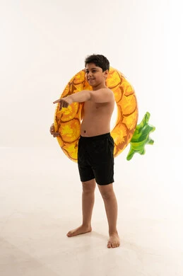 طفل سعودي يحمل طوق سباحة أناناس على خلفية بيضاء