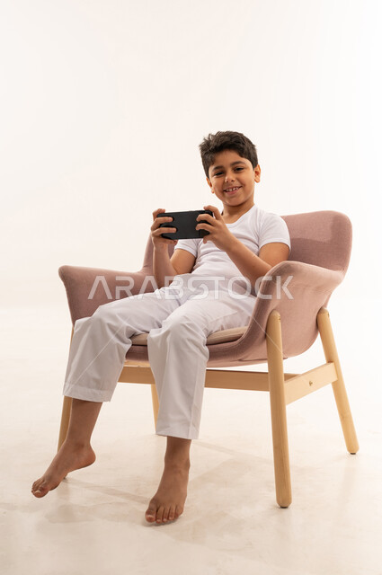 Saudi Boy Using Smartphone in Pink Armchair