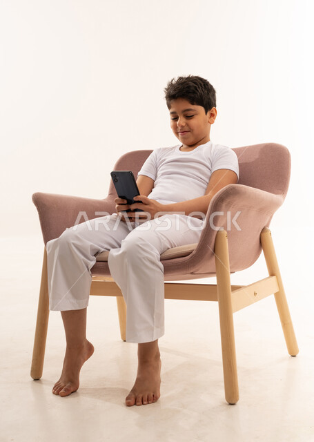 Saudi Boy Using Smartphone in Pink Armchair