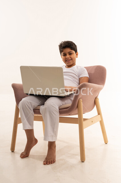 طفل عربي يستخدم لابتوب على كرسي بخلفية بيضاء
