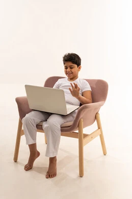 طفل عربي يلوح لجهاز لابتوب على كرسي وردي