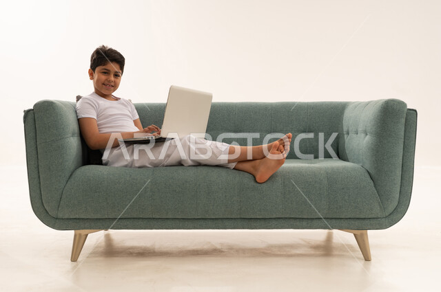Arab Boy Using Laptop on Teal Sofa Studio Shot