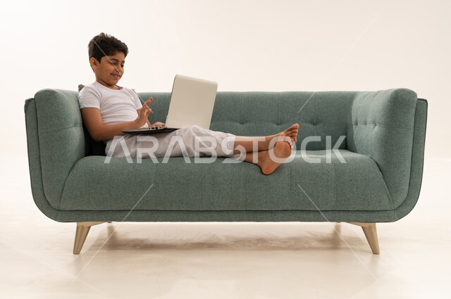 Arab Boy Using Laptop on Modern Teal Sofa