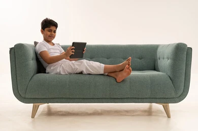 طفل سعودي يستخدم جهاز لوحي على أريكة خضراء