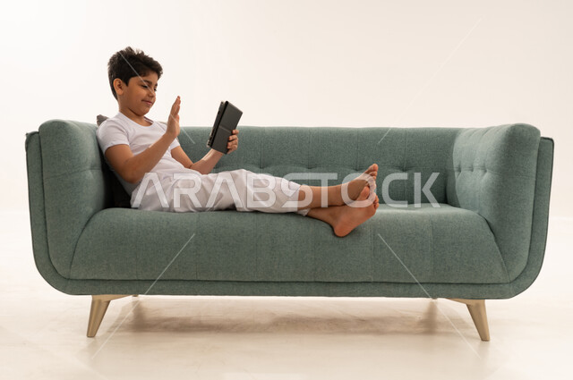 Saudi Boy Waving at Tablet on Green Sofa