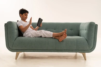 طفل سعودي يلوح لجهاز لوحي على أريكة خضراء