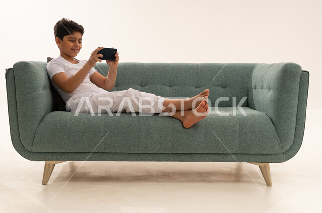 طفل سعودي يلعب بالهاتف الذكي على الأريكة