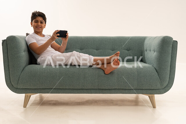 Arab Boy Using Smartphone on Green Sofa