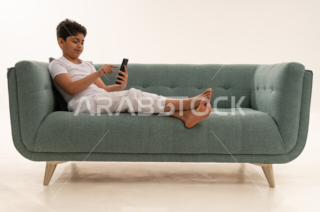 Arab Boy Using Smartphone on Modern Green Sofa